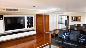 A modern living room with a flat-screen TV, a black leather sofa, and a dining area with a wooden table and chairs.