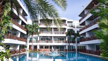 A multi-story hotel with a central swimming pool, balconies, and palm trees.