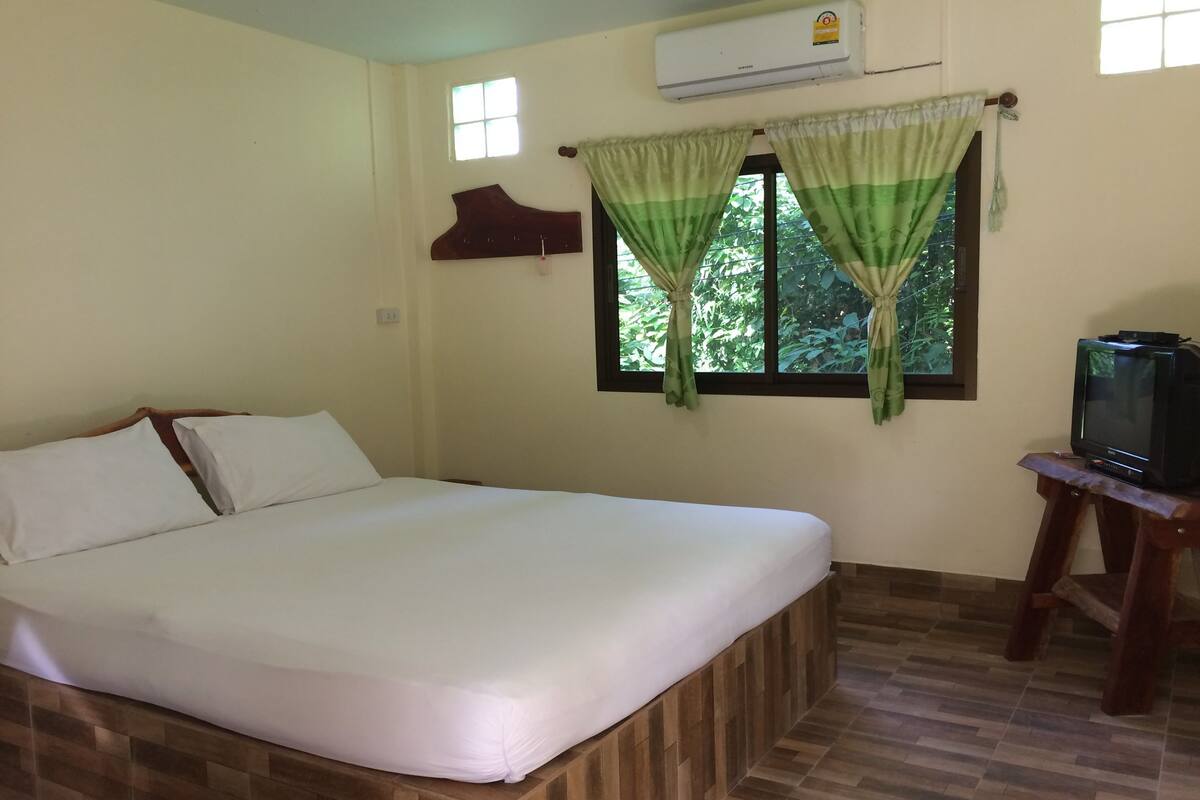 A bedroom with a bed, a television on a wooden stand, and a window with curtains.
