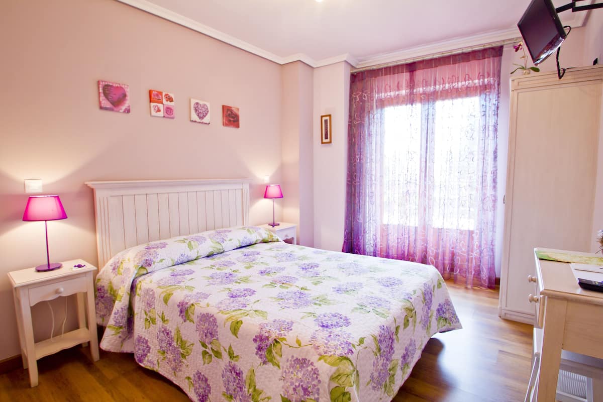 A bedroom with a bed, bedside lamps, a wardrobe, and a TV on a stand.