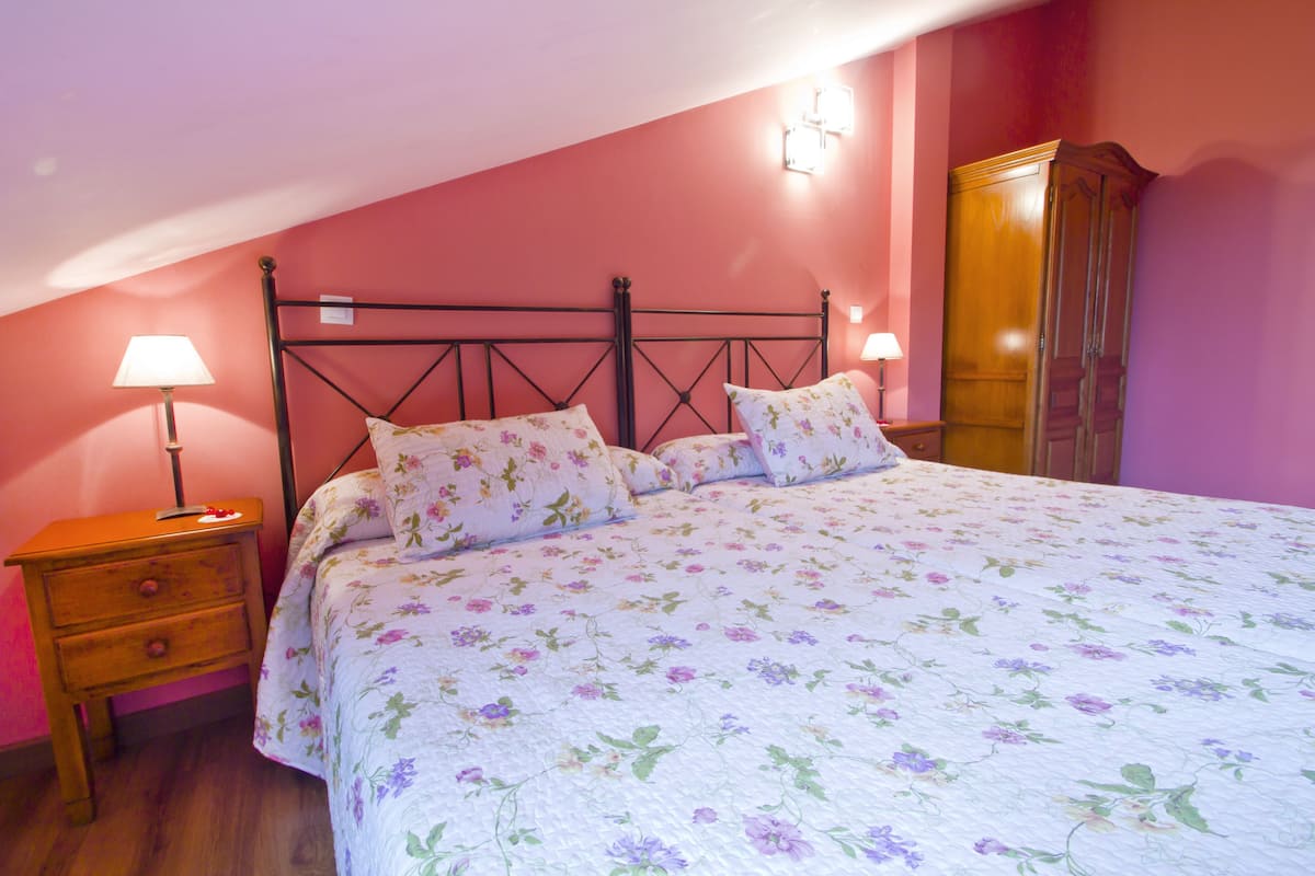 A bedroom with a bed, two bedside tables, a nightstand, a wardrobe, and two wall-mounted lamps.