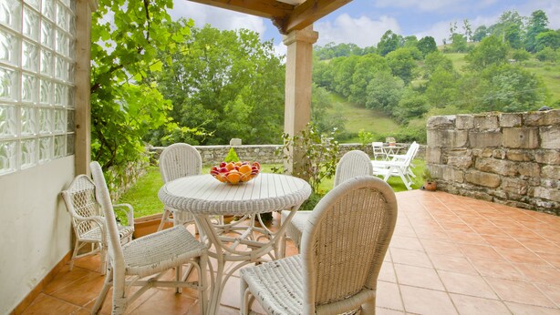 A covered patio with wicker furniture and a stone wall. - Posada de Villacarriedo (Villacarriedo)