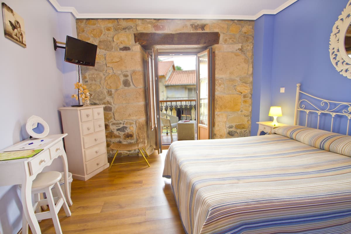 A bedroom with a bed, a desk, a chair, a dresser, a television, and a stone wall.