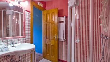 A bathroom with a sink, mirror, shower, and a door leading to another room.