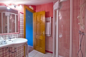 Een badkamer met een wastafel, spiegel, douche en een deur naar een andere ruimte.