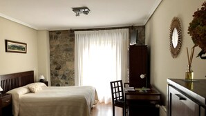 A bedroom with a bed, a desk, a chair, a dresser, a mirror, and a stone wall. - Posada de Villacarriedo (Villacarriedo)