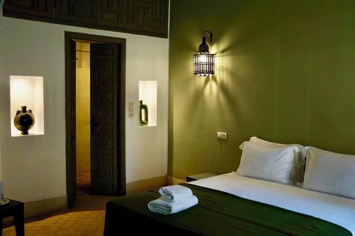 A hotel room with a bed, a nightstand, a lamp, and a door.