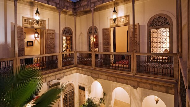 A courtyard with ornate wooden balconies, arched doorways, and decorative lighting fixtures. - Riad Tzarra (Marrakech)