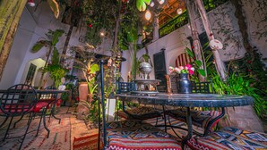 An indoor garden with a round table, chairs, and various plants. - Riad Tibibt (Marrakech)