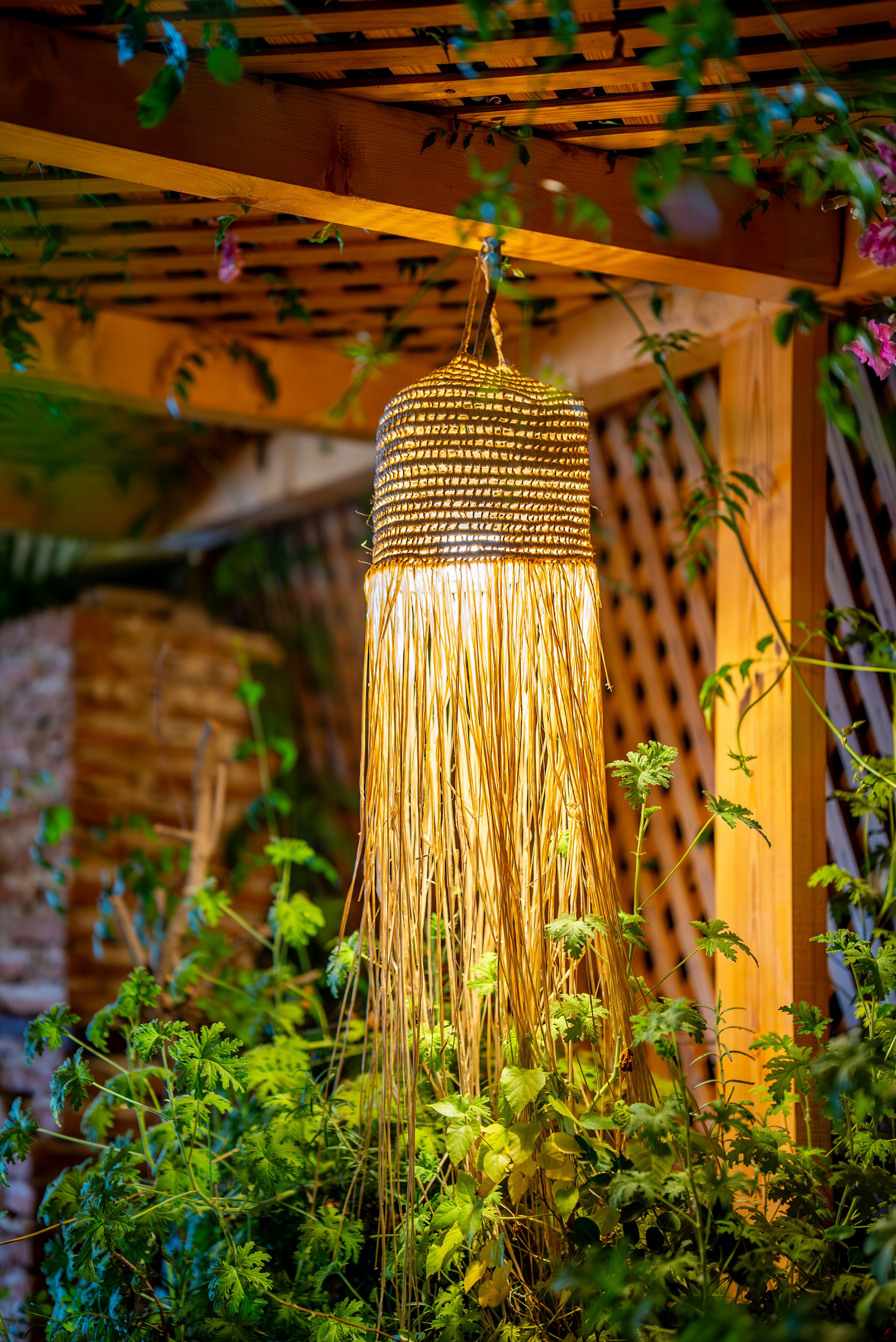 A hanging lantern with a tassel, surrounded by greenery and a wooden structure.