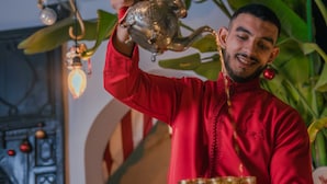 A person in a red traditional outfit holding a tray with a teapot and cups. - Riad Tibibt (Marrakech)