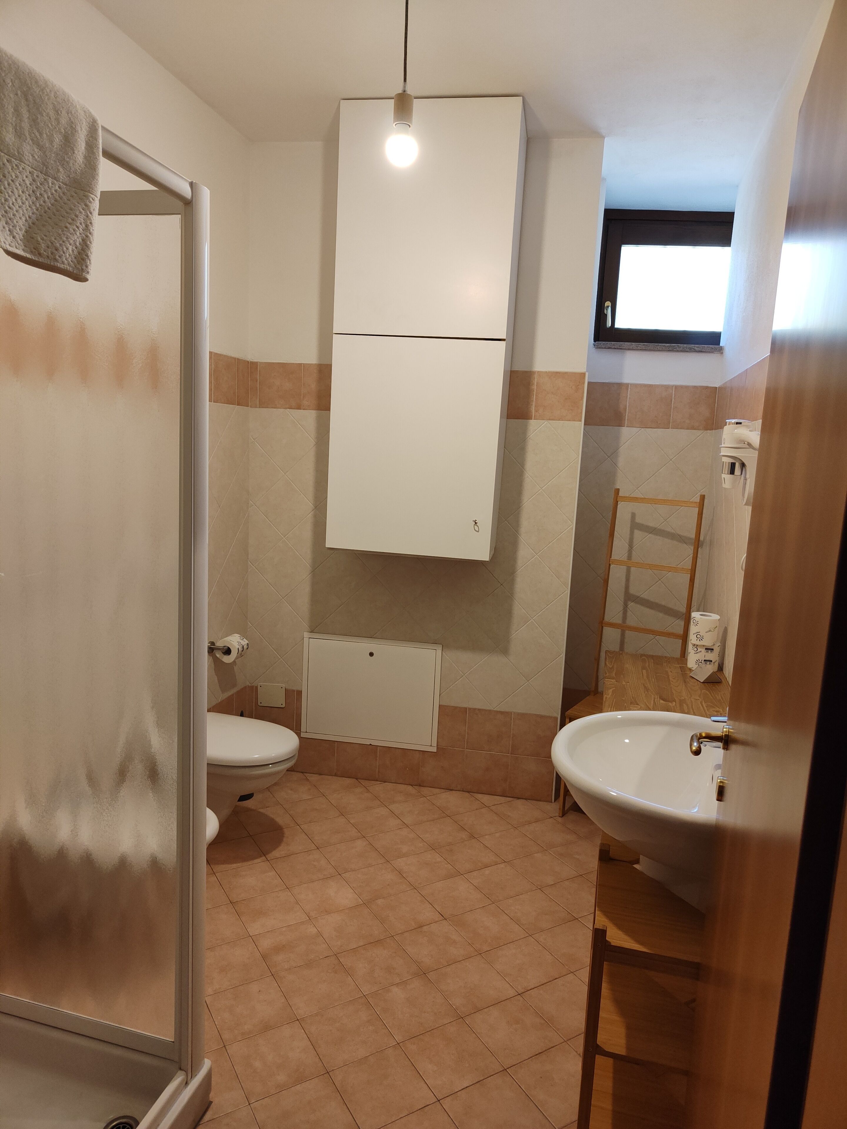 A bathroom with two toilets, a sink, a mirror, and a towel hanging on the wall.