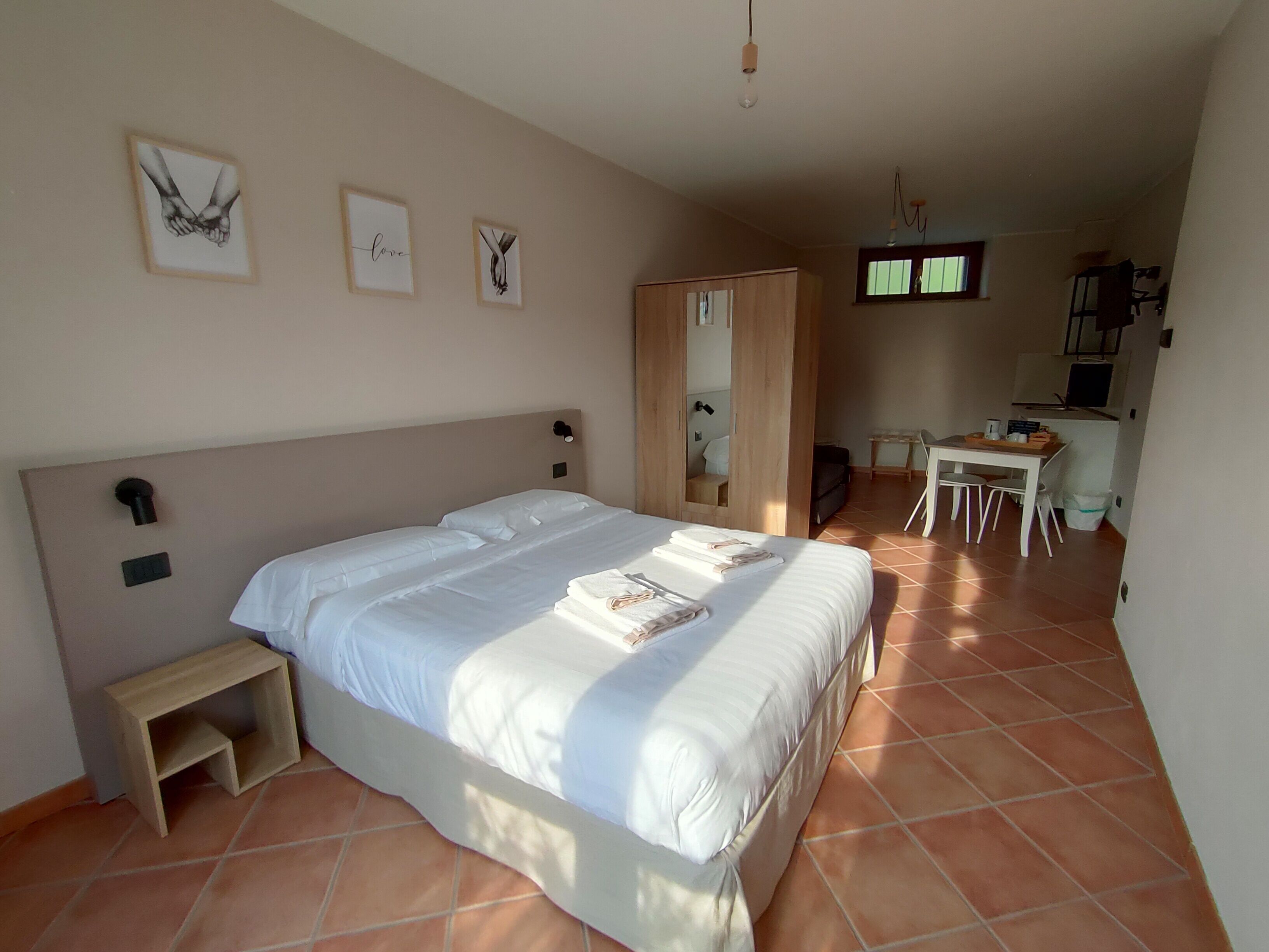 A bedroom with a large bed, a small bedside table, a desk with a chair, a television, and a wardrobe.