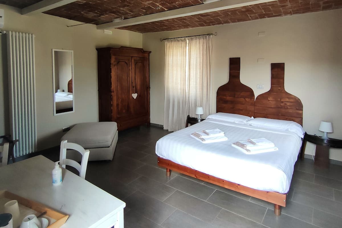 Hotelkamer met bakstenen plafond, een bed met witte lakens, een houten hoofdeinde, een houten kledingkast, een tafeltje met een dienblad en een stoel.