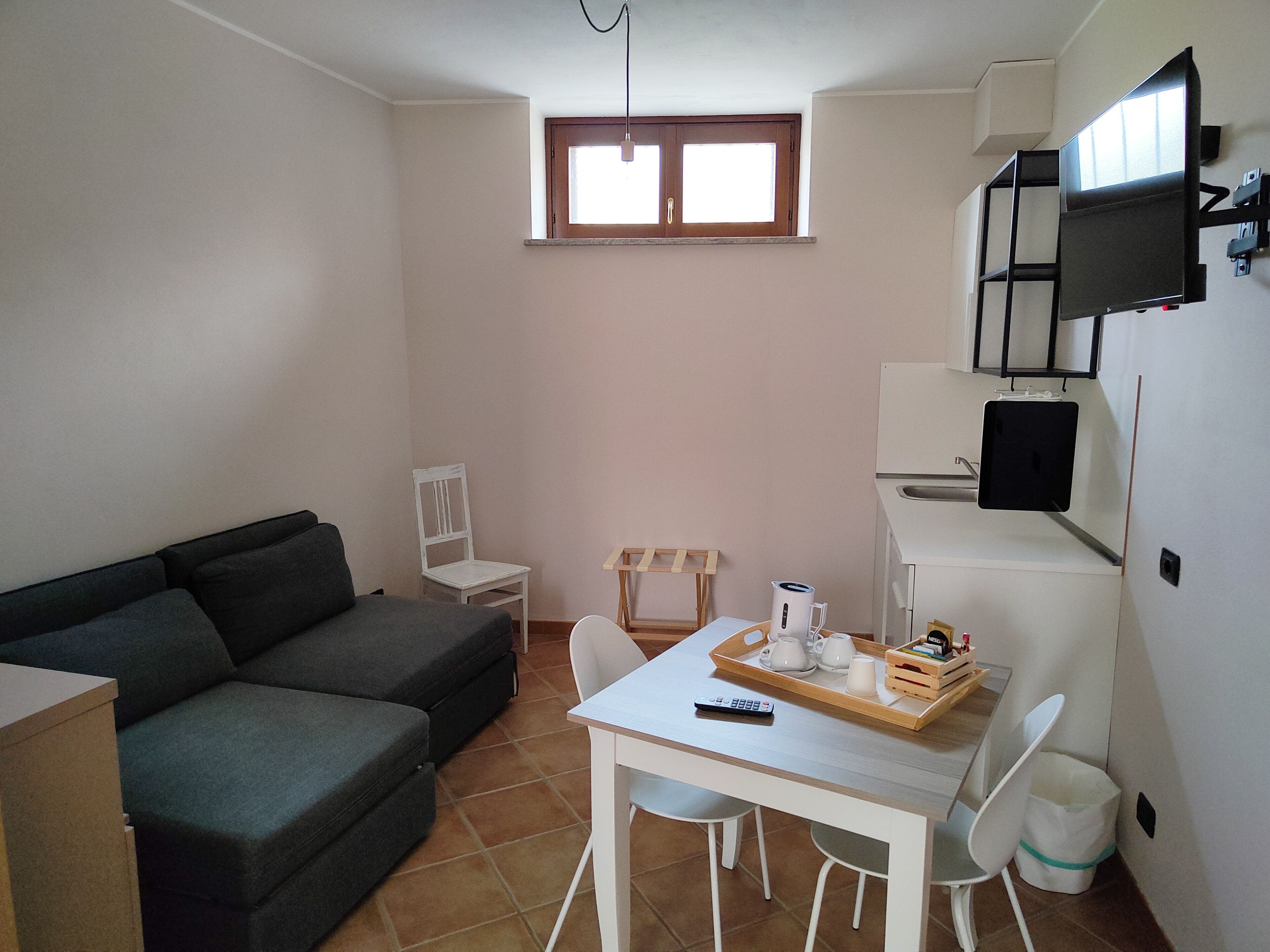 Un espacio habitable pequeño y funcional con sofá, una mesa de comedor con sillas, una ventana pequeña y un televisor montado en la pared.