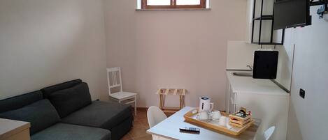 Un espacio habitable pequeño y funcional con sofá, una mesa de comedor con sillas, una ventana pequeña y un televisor montado en la pared.