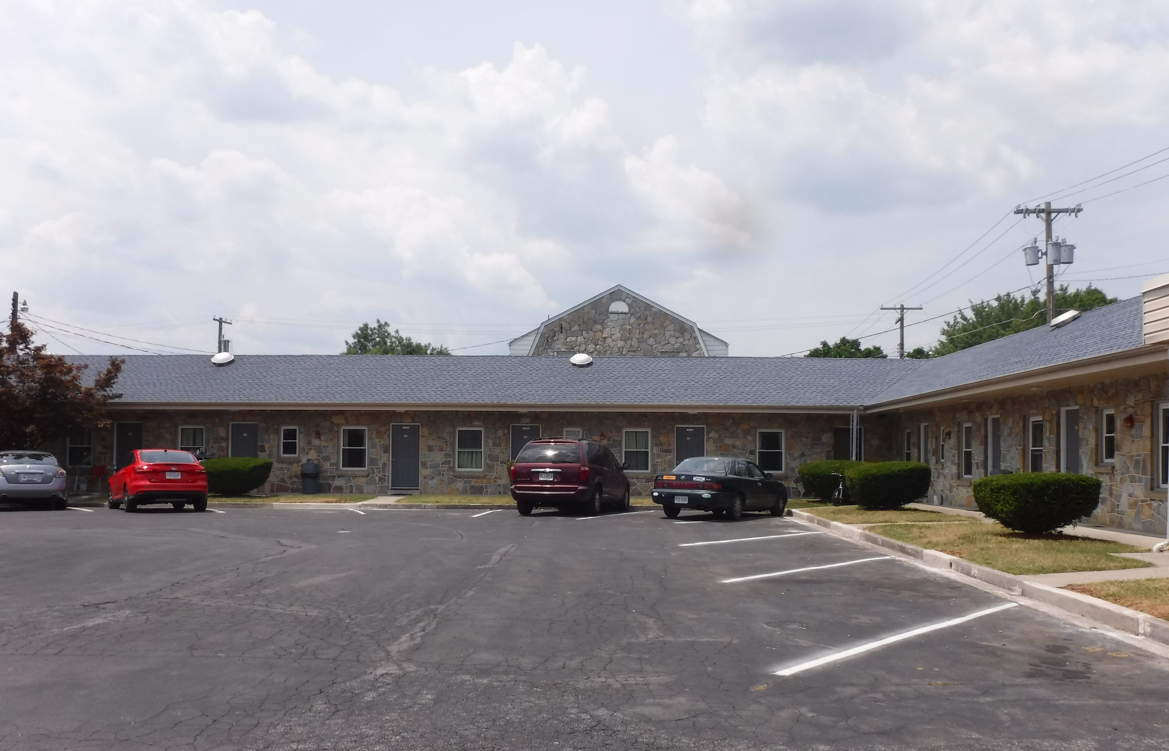 A motel with a stone facade, a parking lot, and a clear sky.