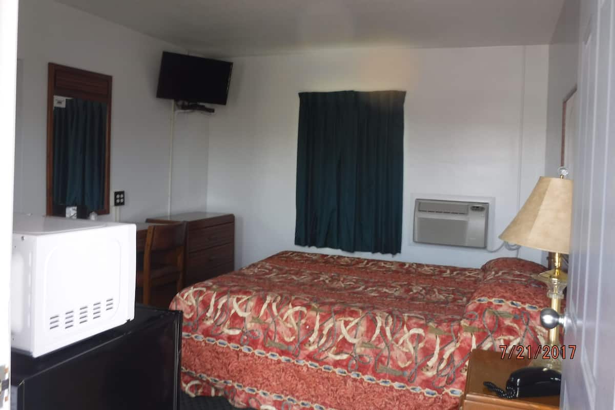 A hotel room with a bed, a television, an air conditioning unit, a desk, and a lamp.