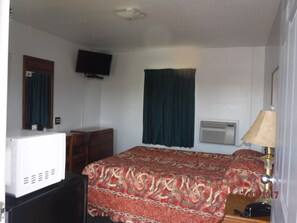 A hotel room with a bed, a television, an air conditioning unit, a desk, and a lamp. - Blue Ridge Motel (Front Royal)