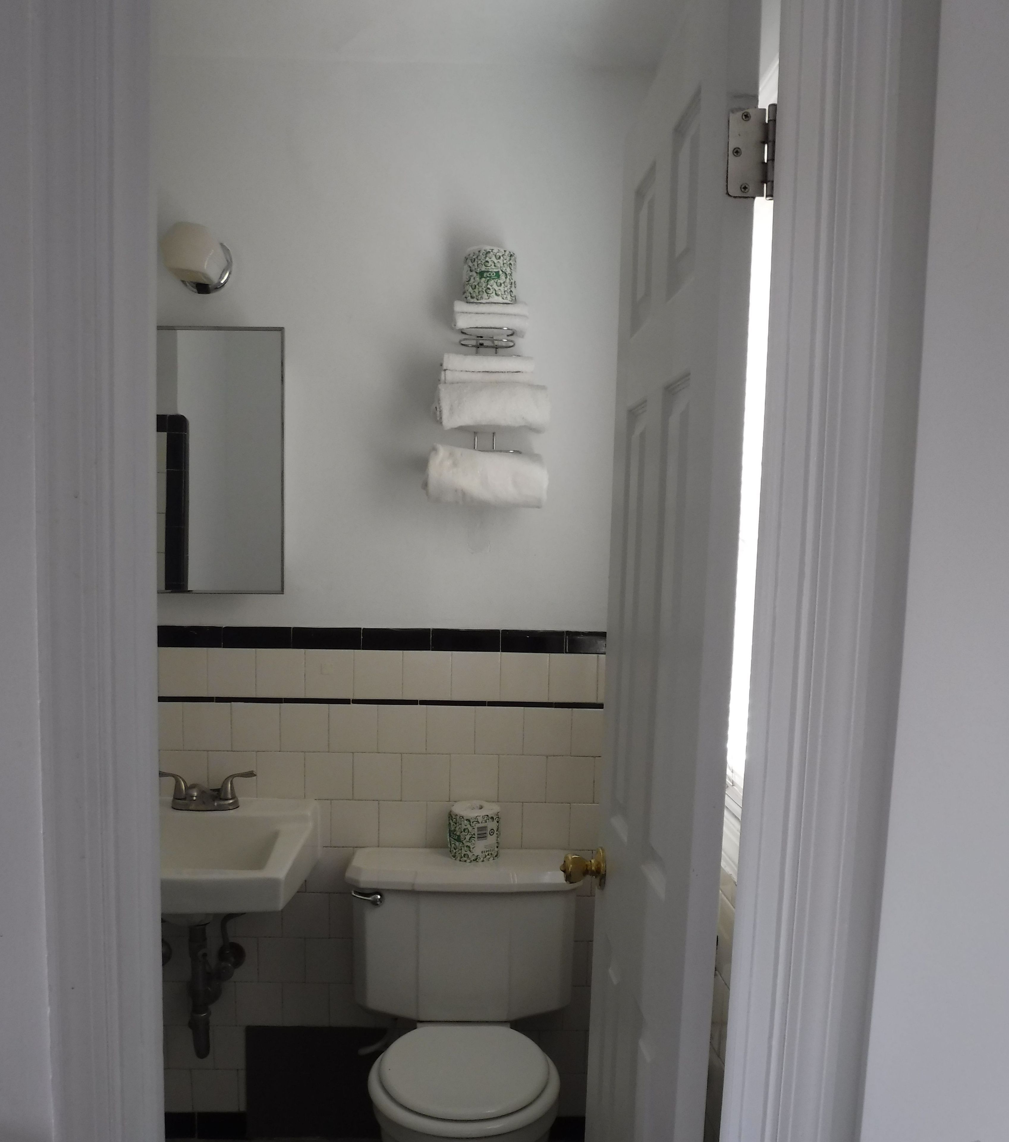 A small, compact bathroom with a toilet, sink, and a towel rack with multiple towels.