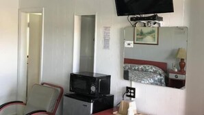 Habitació petita i senzilla amb bugateria, un llit individual, televisió penjada a la paret i mirall sobre el llit.