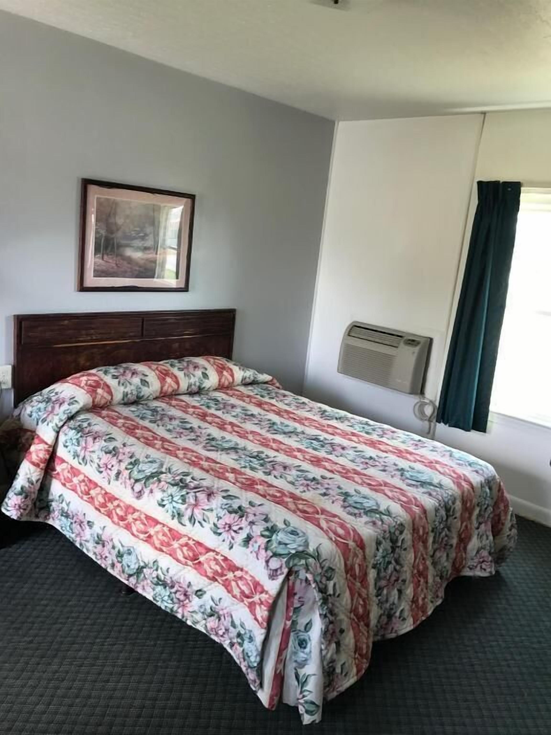 A hotel room with a bed, a framed picture on the wall, and a window with curtains.