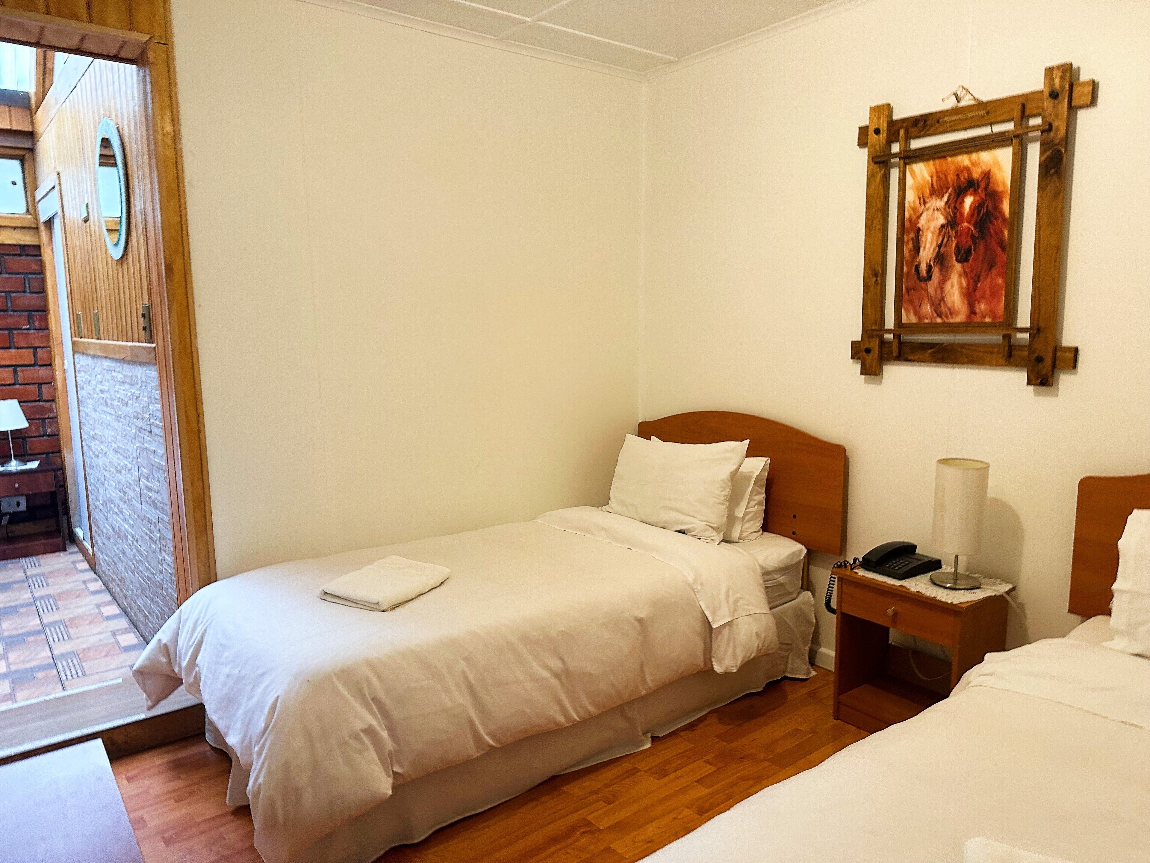 Una cama individual con cabecera de madera, una mesita de noche con lámpara y un cuadro en la pared.