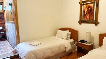Una cama individual con cabecera de madera, una mesita de noche con lámpara y un cuadro en la pared.