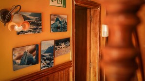 Um corredor com uma porta de madeira, um candeeiro fixado na parede e várias fotografias emolduradas de paisagens geladas.