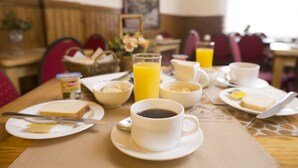 Uma mesa de café da manhã montada para duas pessoas, com pratos, pão, manteiga, geleia, uma xícara de café e um copo de suco de laranja.