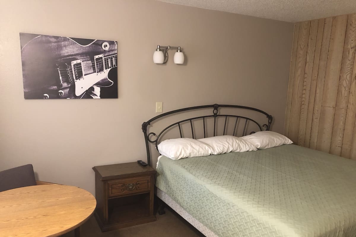 A bedroom with a bed, a nightstand, a chair, and a wall-mounted lamp.