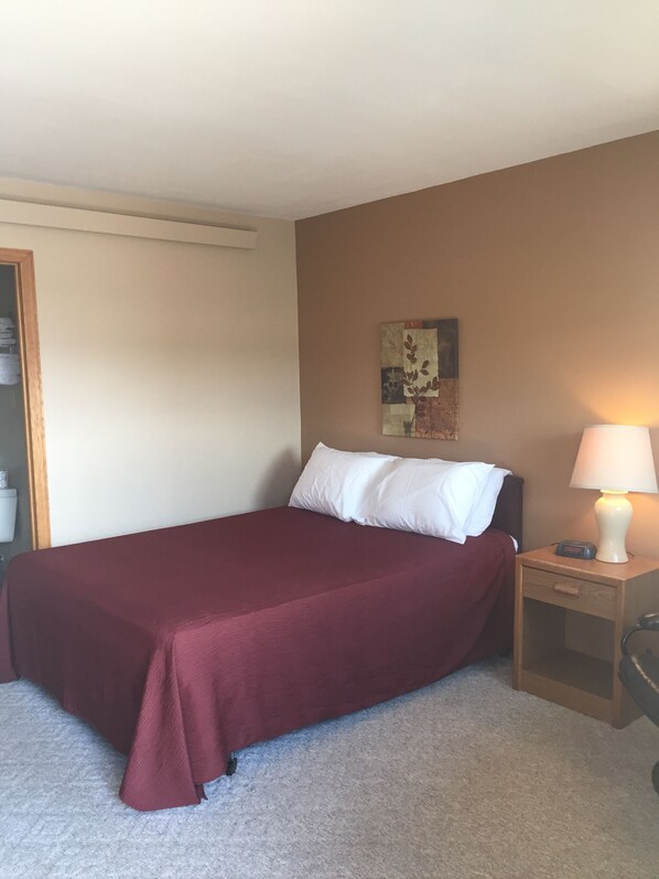 A single bed with a red bedspread and white pillows, a bedside table with a lamp, and a wall-mounted artwork. - King's Inn (Kennebec)
