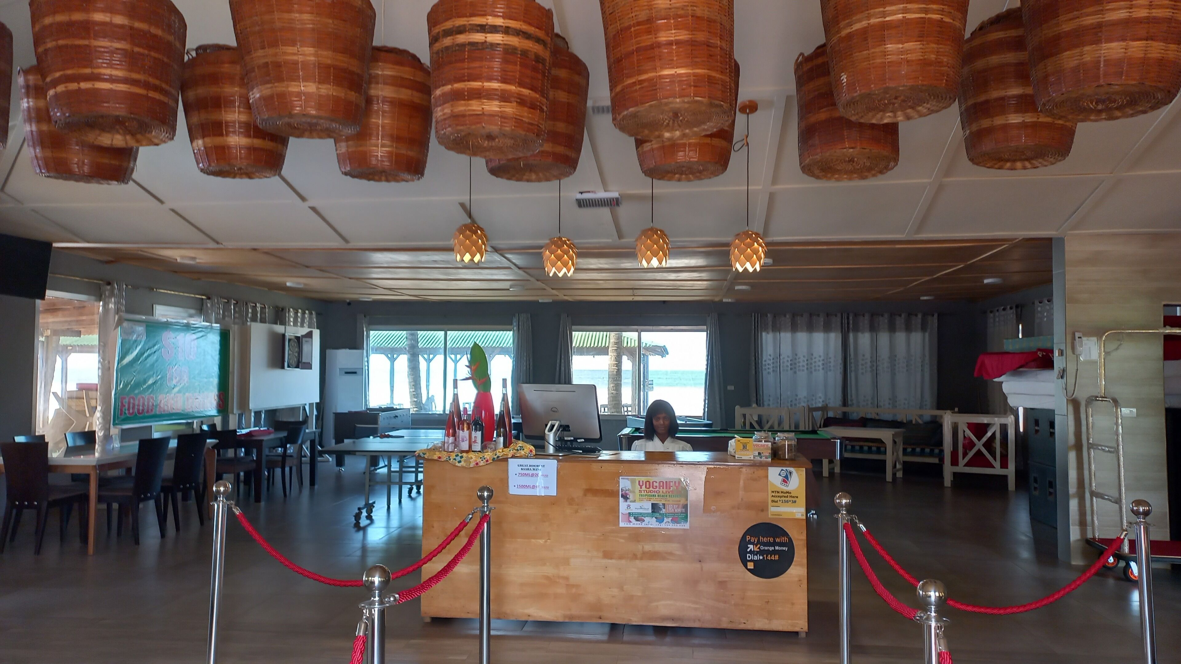 A hotel lobby with a reception desk, wooden flooring, and hanging wicker lamps.