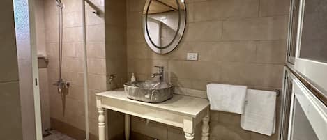 A bathroom with a wooden ceiling, a round mirror, a sink, a toilet, and a shower.