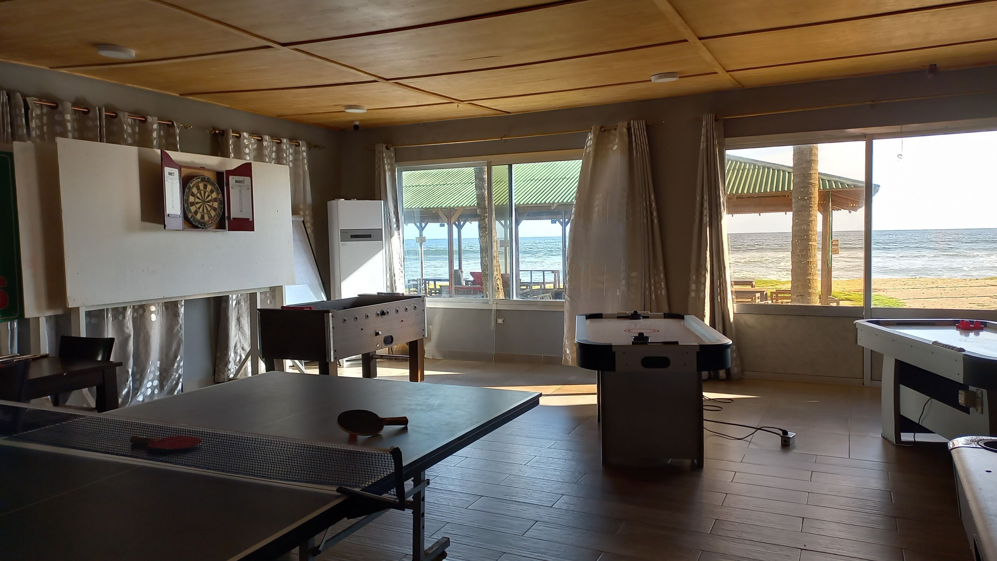 Een kamer met een pingpongtafel, een tafelvoetbalspel en een dartbord. Er is een raam met uitzicht op het strand en de oceaan.
