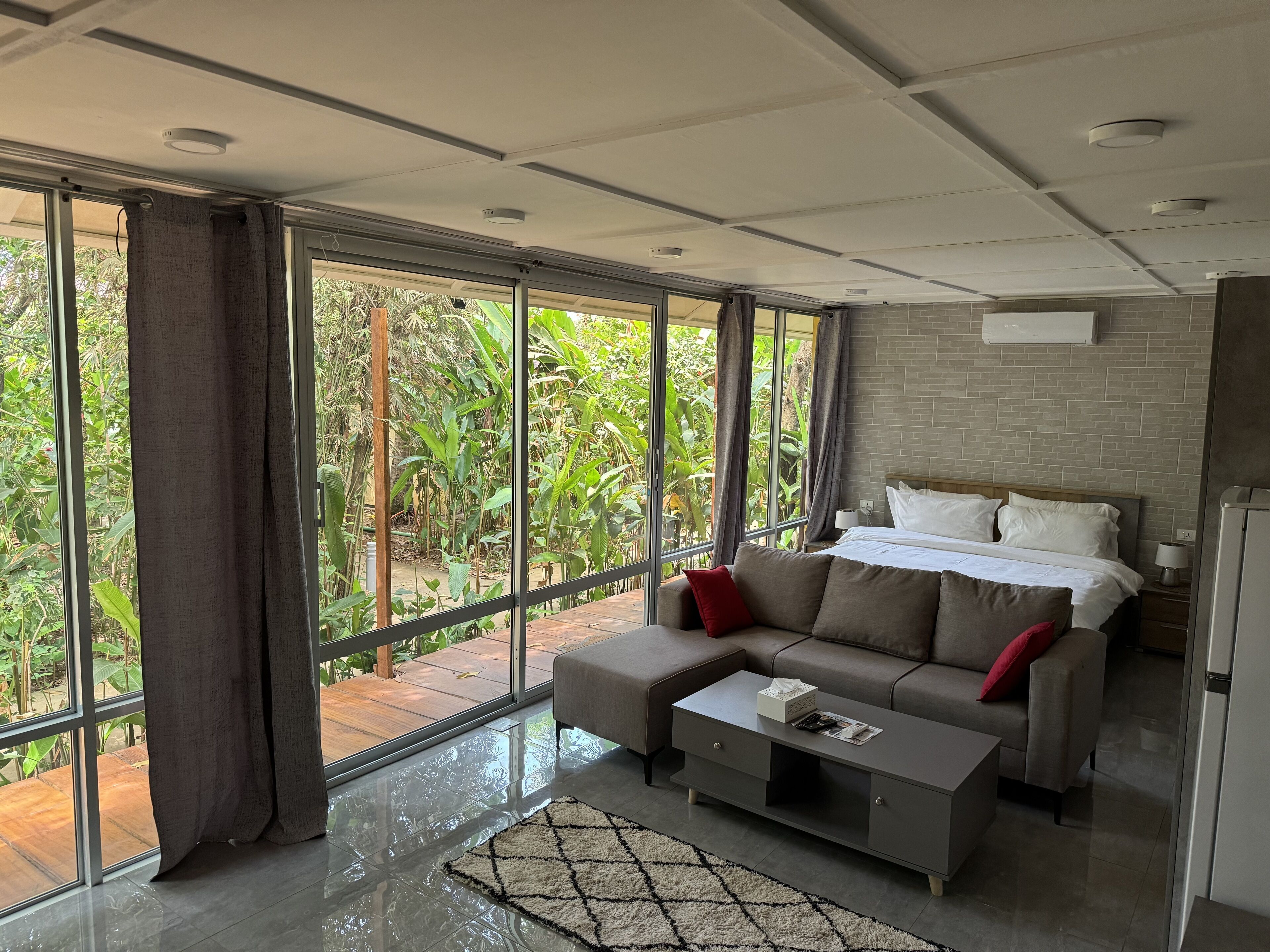 A modern hotel room with a large window, a sofa, a coffee table, and a bed with white bedding.