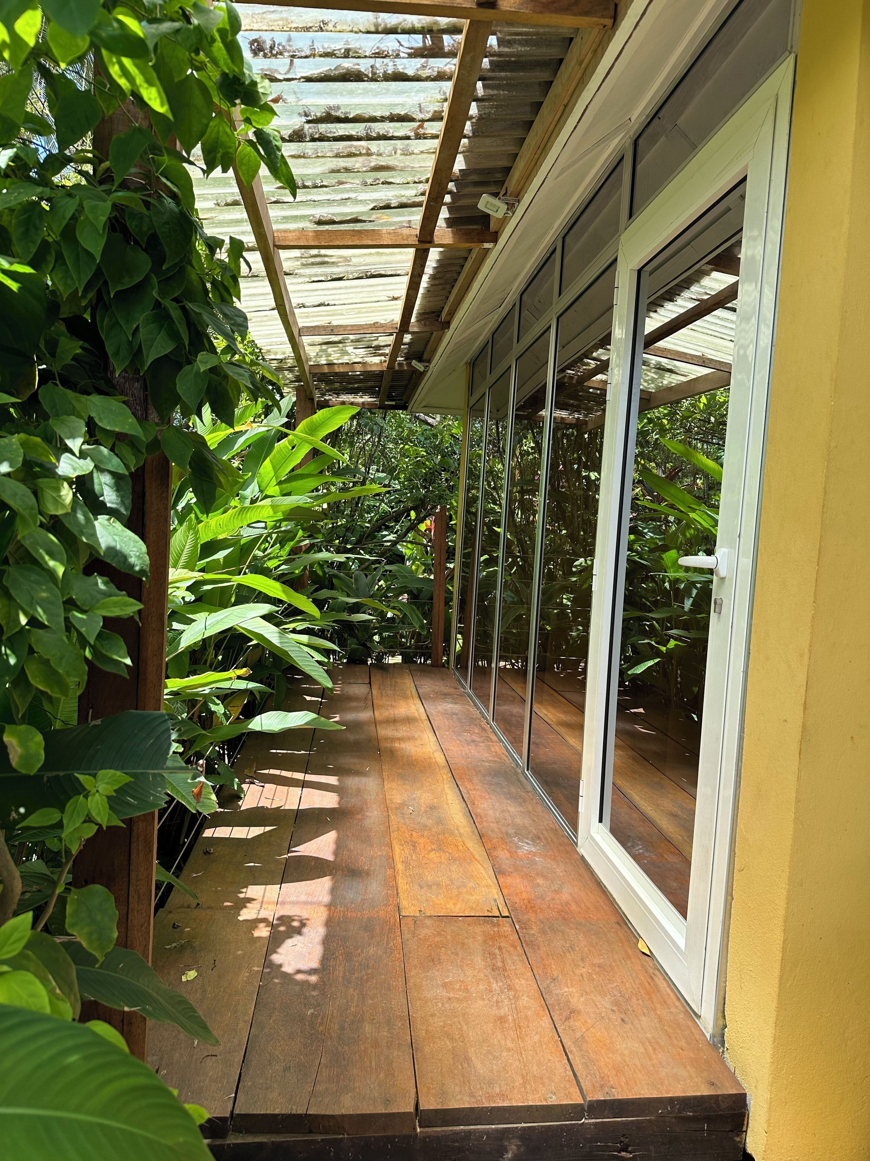 A covered wooden deck with glass doors leading to a lush garden area.