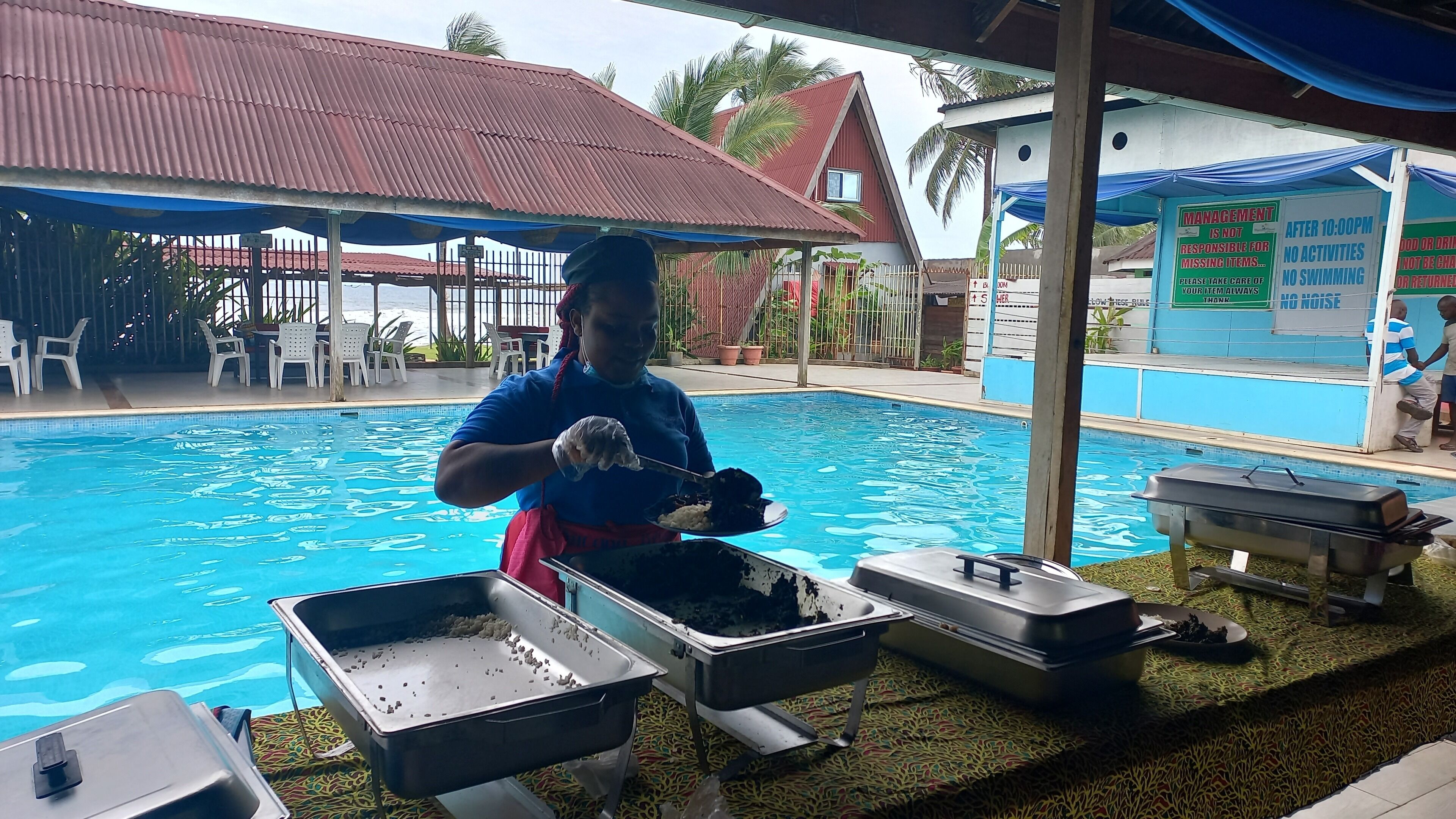 Un buffet a bordo piscina con contenitori per alimenti e una persona che serve.