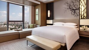 Quarto de hotel moderno com uma cama grande, um banco, vista para a cidade e uma parede decorativa.