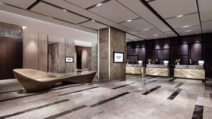 Um hall de hotel moderno com uma mesa de recepção, uma área de estar diferenciada e piso de mármore.