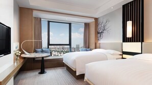 Quarto de hotel com duas camas, área de estar com vista, televisão de tela plana e uma pequena mesa com abajur.