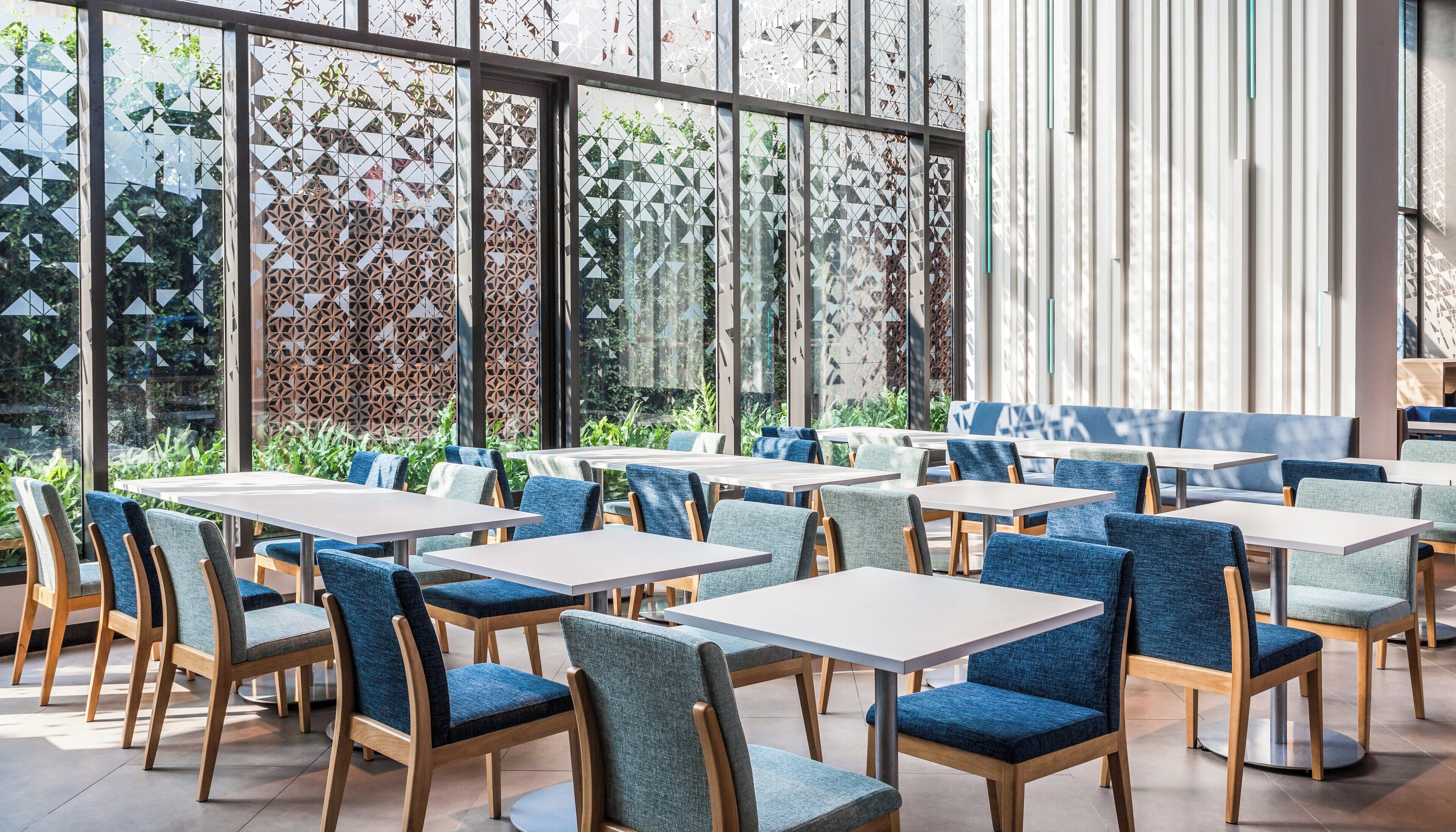 A modern indoor dining area with tables and chairs, large windows, and a patterned wall.