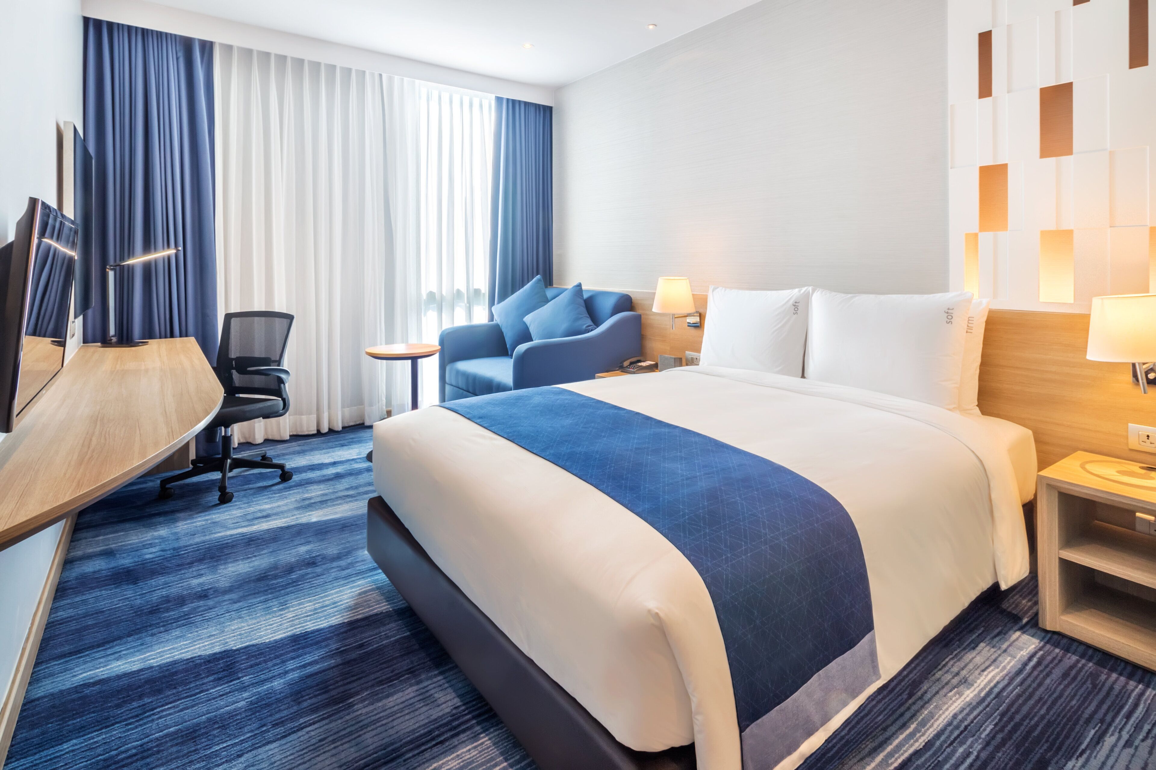 Ein Hotelzimmer mit einem großen Bett, einem Schreibtisch, einem Sessel und einem Fernseher.