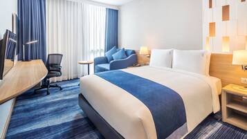 A hotel room with a large bed, a desk, a chair, and a TV.