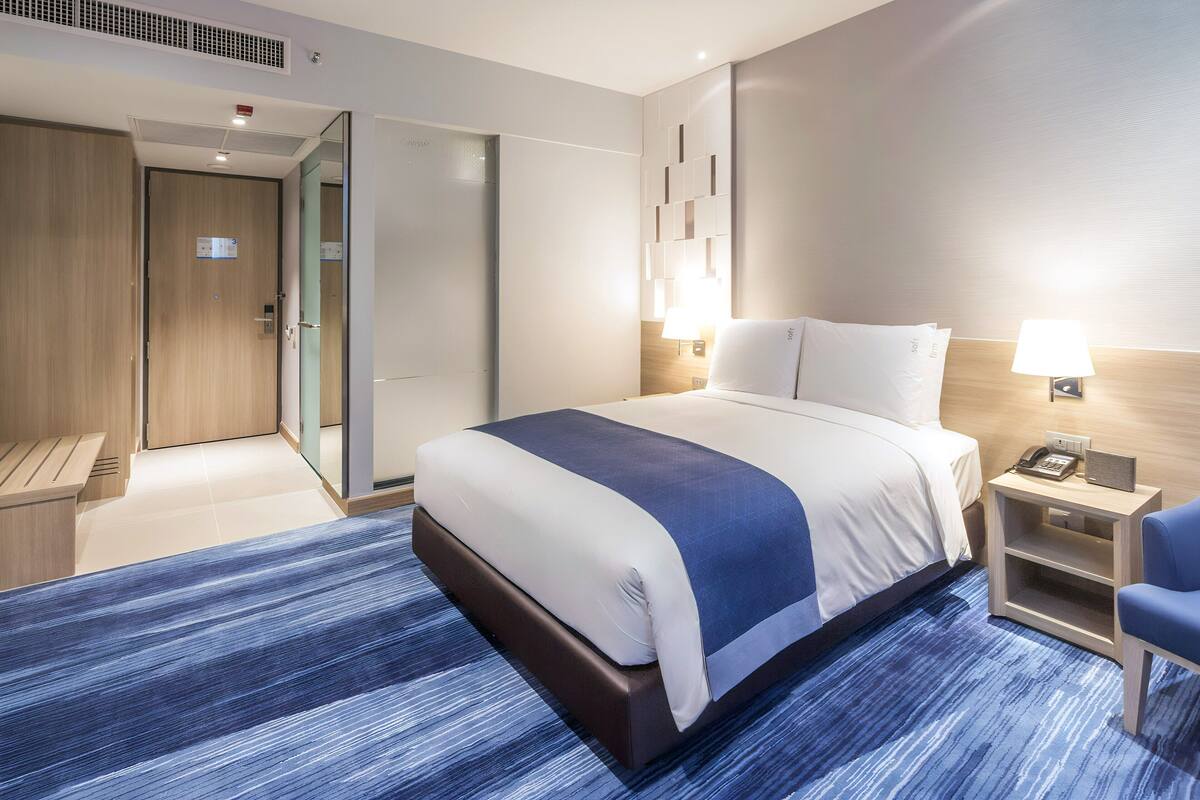 A modern hotel room with a large bed, bedside tables, a desk, and a chair.