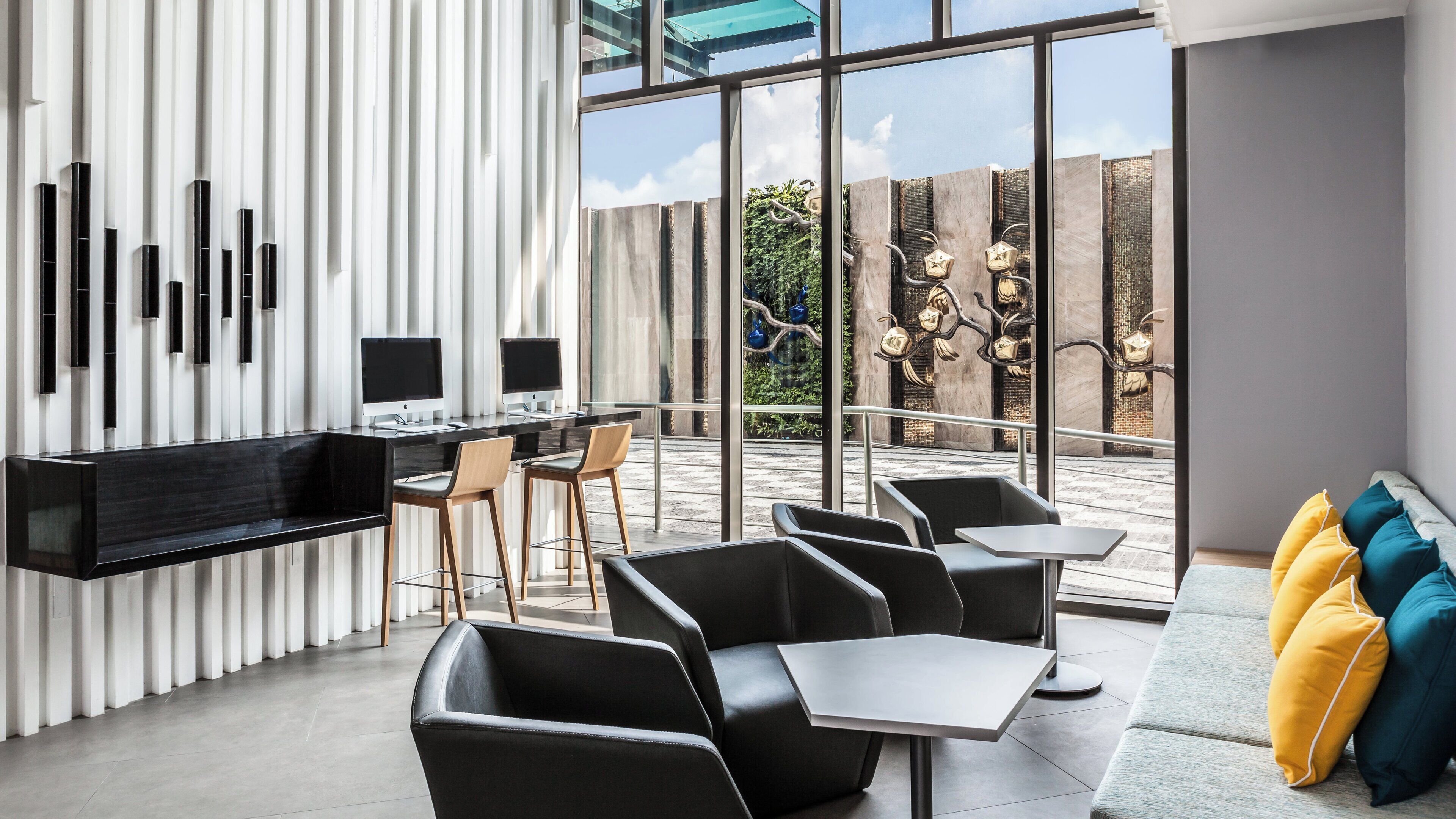 A modern interior with a long dining table, black chairs, and a sofa with colorful cushions.