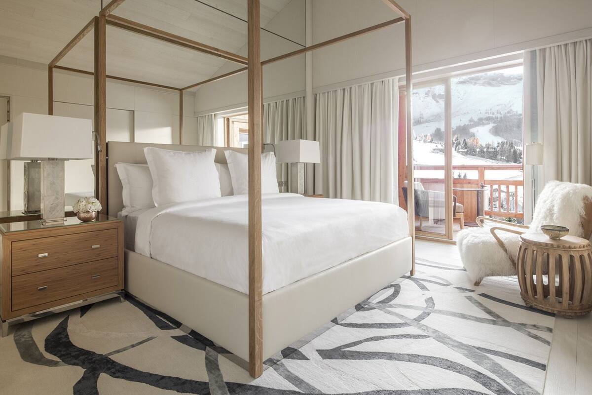 A four-poster bed with a view of a snowy landscape through a balcony.
