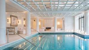 A luxurious indoor pool area with a clear view of the pool, white columns, and seating areas.