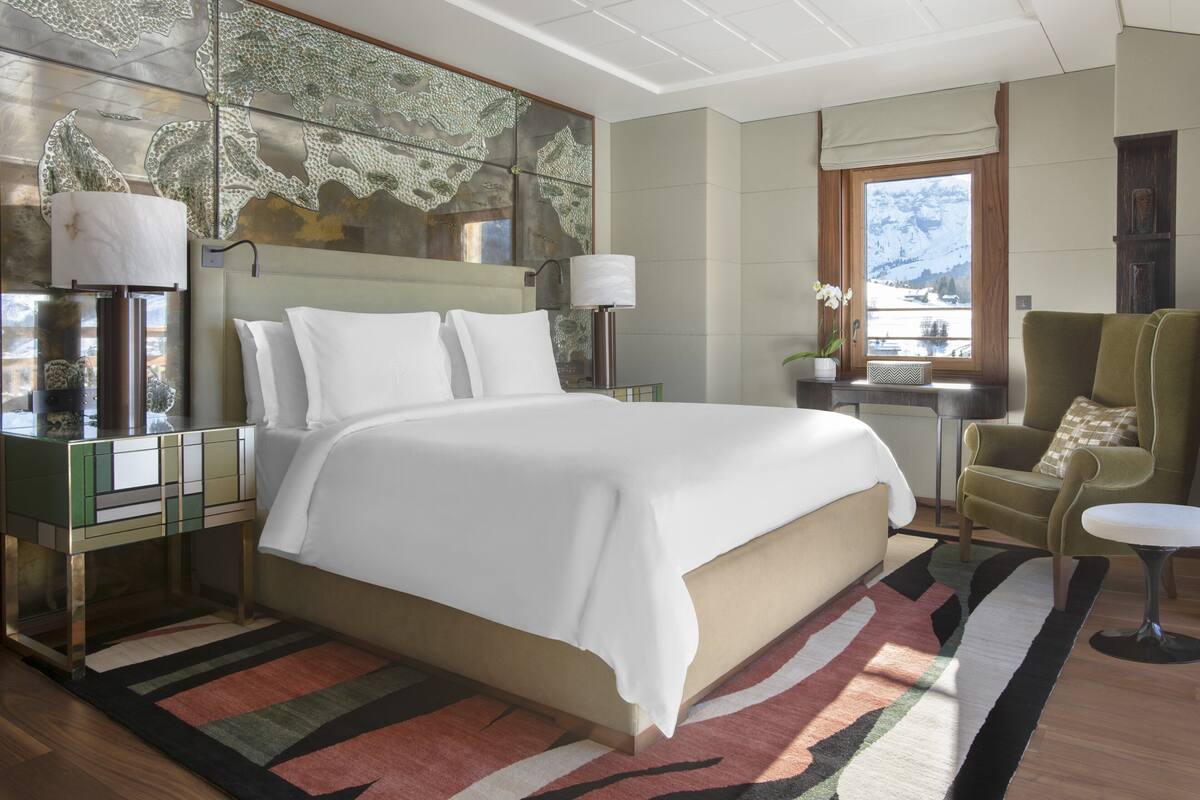 A spacious bedroom with a large bed, a nightstand, a chair, and a view of the outdoors.