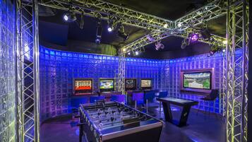 A room with a foosball table, multiple screens, and a blue-lit environment.